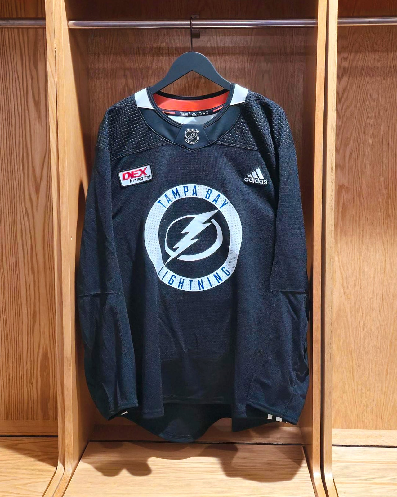 Black practice jersey with Tampa Bay Lightning logo on a wooden locker door.