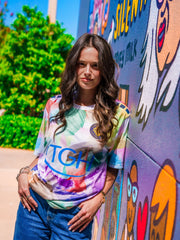 Woman wearing a colorful tie-dye shirt with 'TGIF' text, standing in front of a graffiti wall.